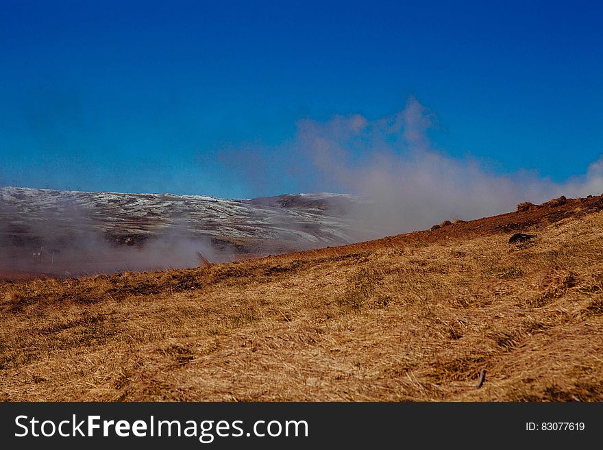 Dry grass covered hillside with smoke rising in background. Dry grass covered hillside with smoke rising in background.