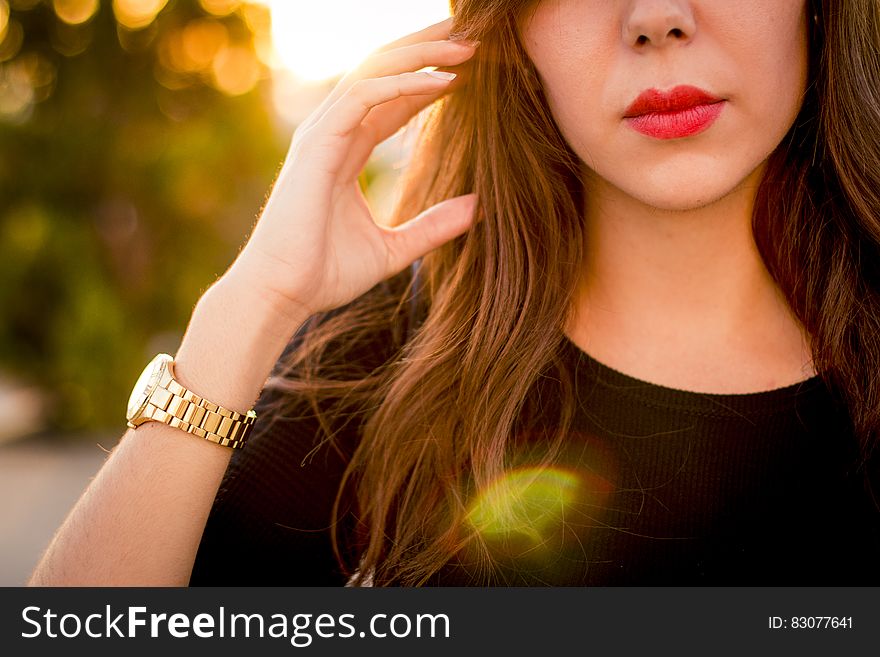 Lower face of beautiful young woman with red lipstick wearing wristwatch outdoors.