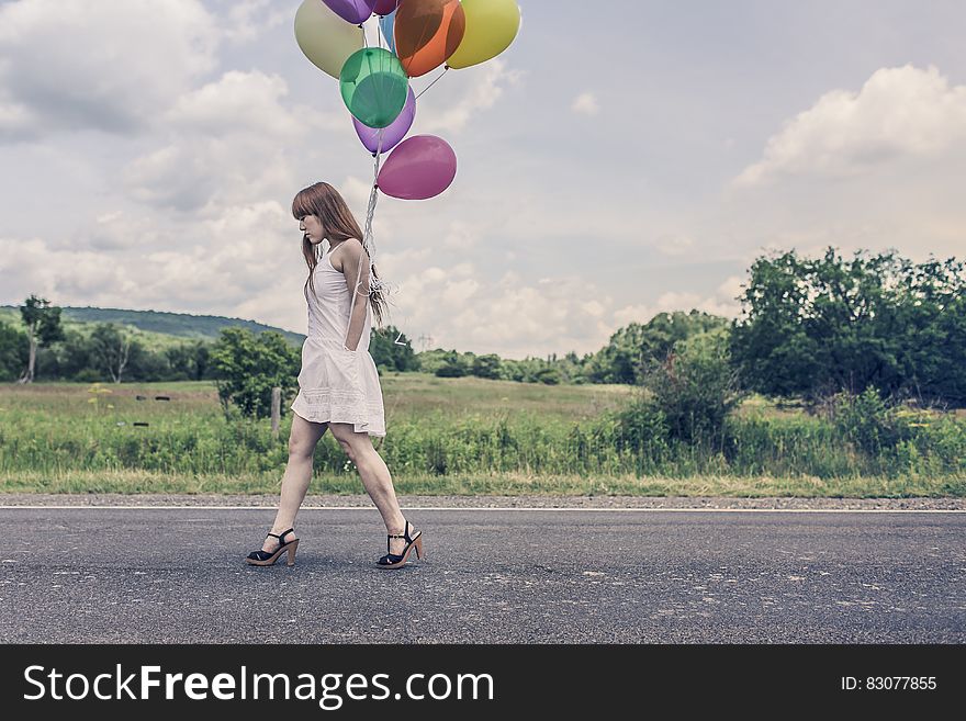 A sad woman is walking with a bunch of balloons. A sad woman is walking with a bunch of balloons.