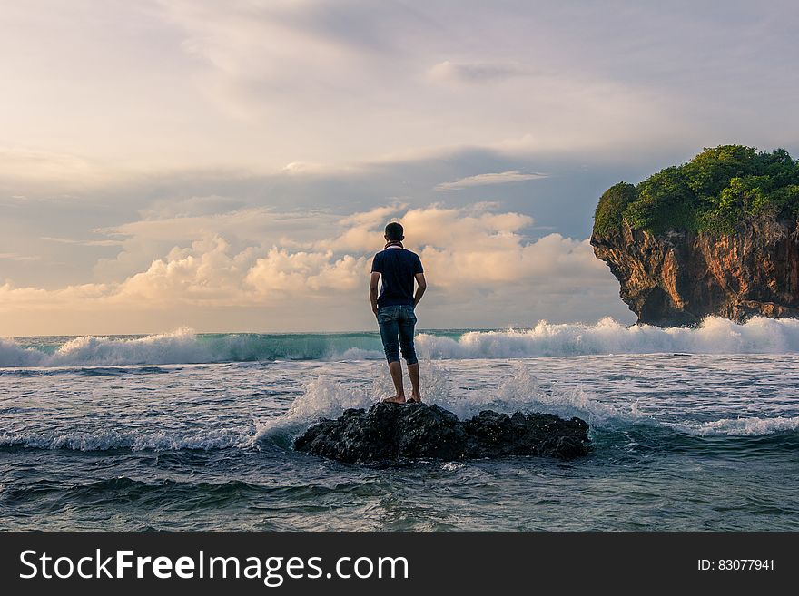 Man Standing on Stone Near Seashore during Sunrise Photography