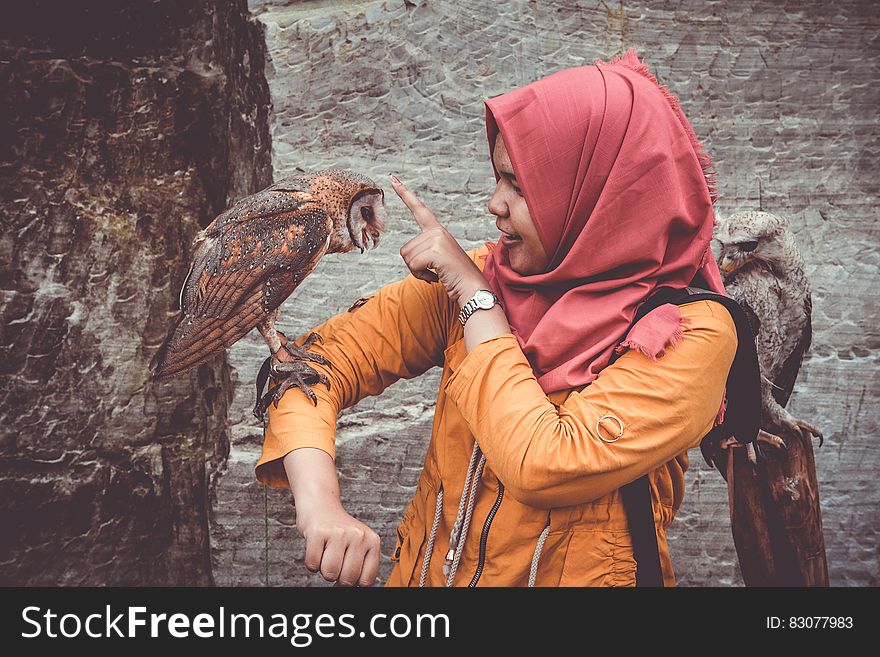 Woman in Red Hijab and Orange Coat Touching Brown and White Owl