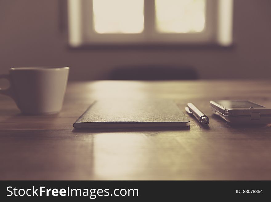 Working desk with notebook, pen and smartphone next to a coffee cup