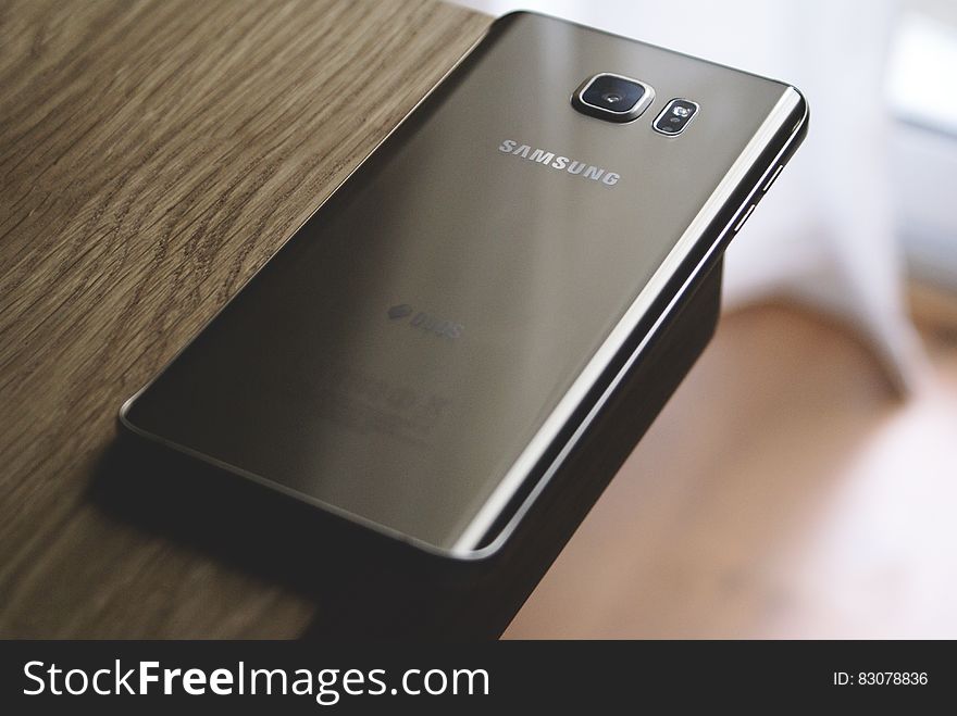 Silver Samsung Galaxy Smartphone on Top of Brown Wooden Table