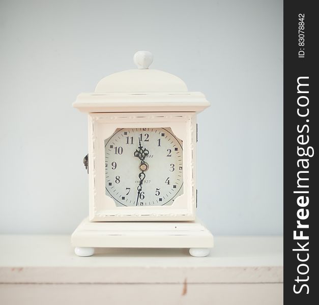 A white antique clock situated on a shelf. A white antique clock situated on a shelf