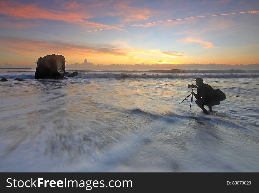 Photographer shooting sunset at the seaside with camera on tripod in the water