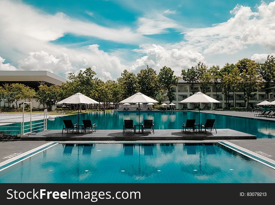 Black Outdoor Lounge Chair in Between Blue Swimming Pool Under White Cloudy Blue Sky