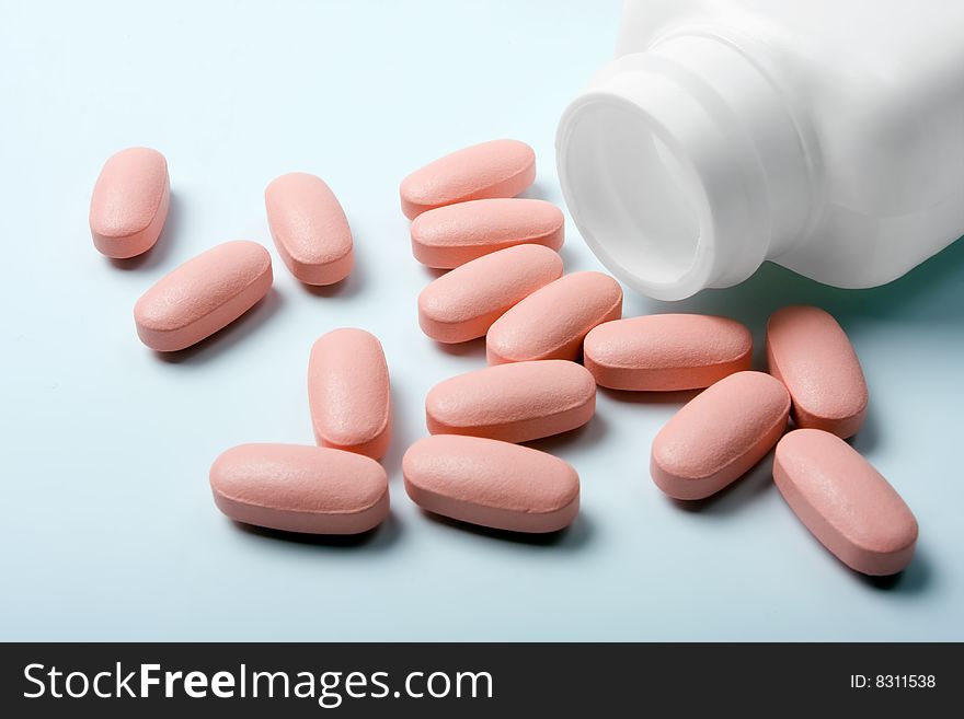 Close-up of pills scattered around the white bottle on a green background. Close-up of pills scattered around the white bottle on a green background