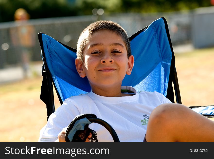 A young boy sitting in a blue chair on a public playground. A young boy sitting in a blue chair on a public playground