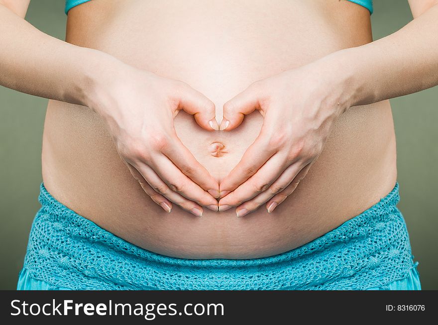 Female hands forming heart over belly