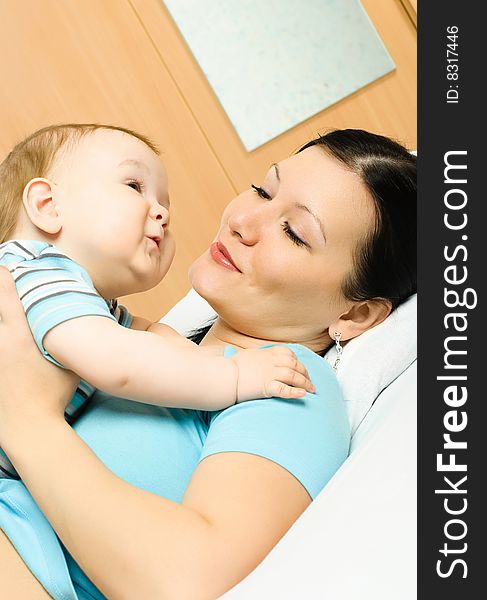 Young mother lies on the bed with her ten months old baby. Young mother lies on the bed with her ten months old baby