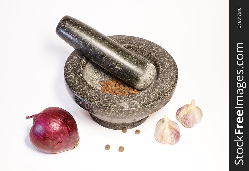 Still life with a granit mortar, spices, garlic and onions on a white background