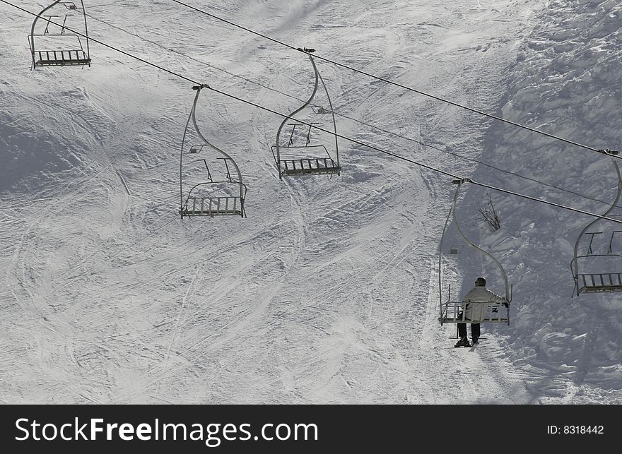 Seen from behind a man sitting on chairlift above snow in the sun. Seen from behind a man sitting on chairlift above snow in the sun.