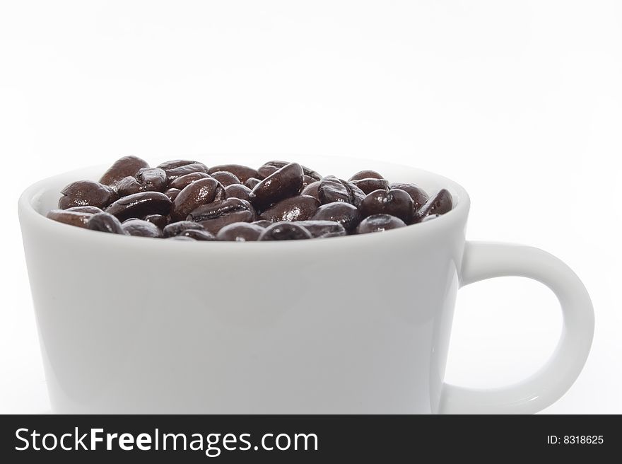 Frontal view of a white cup of coffee beans. Light from above left; reflection in beans.