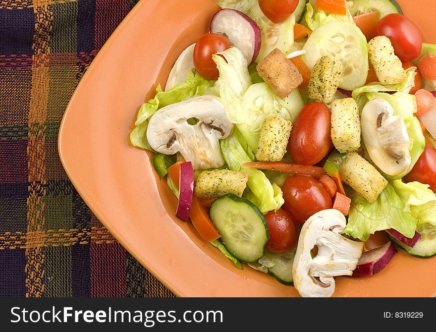 A closeup image of a fresh garden salad with mushrooms in orange bowl on a plaid fall colored mat  copy space. A closeup image of a fresh garden salad with mushrooms in orange bowl on a plaid fall colored mat  copy space
