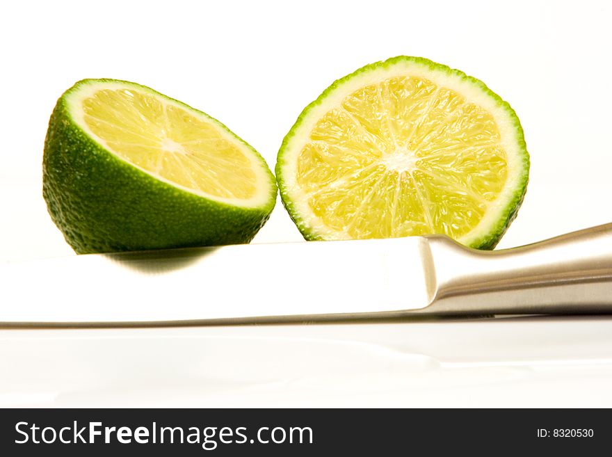 High key image of a sliced lime and a stainless steel knife on a white background. High key image of a sliced lime and a stainless steel knife on a white background