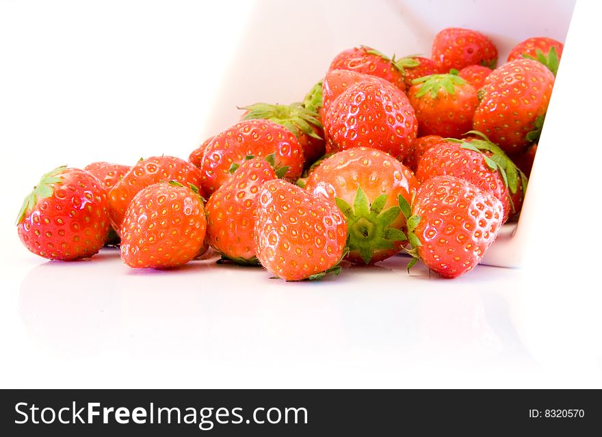 High key image of a collection of strawberries spilling from a white bowl on a white background. High key image of a collection of strawberries spilling from a white bowl on a white background