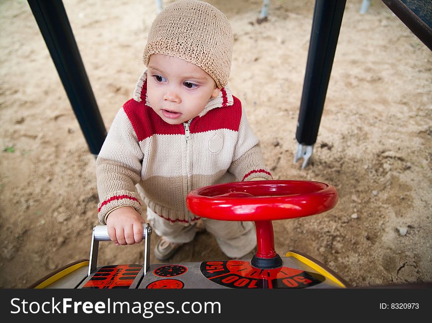 A young child playing with a driving toy on a playground. . A young child playing with a driving toy on a playground.