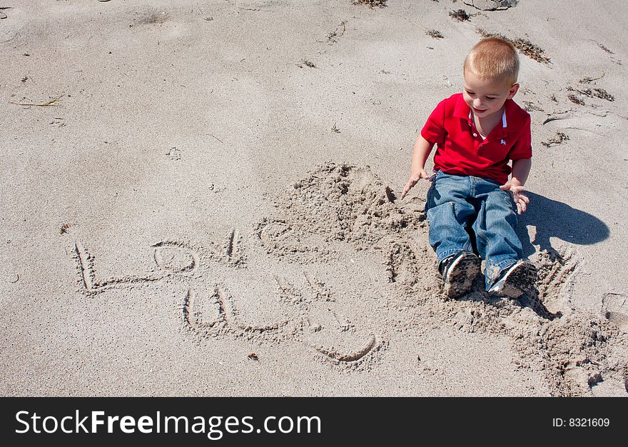 A 2 year old boy playing in the sand with the words love u. A 2 year old boy playing in the sand with the words love u.