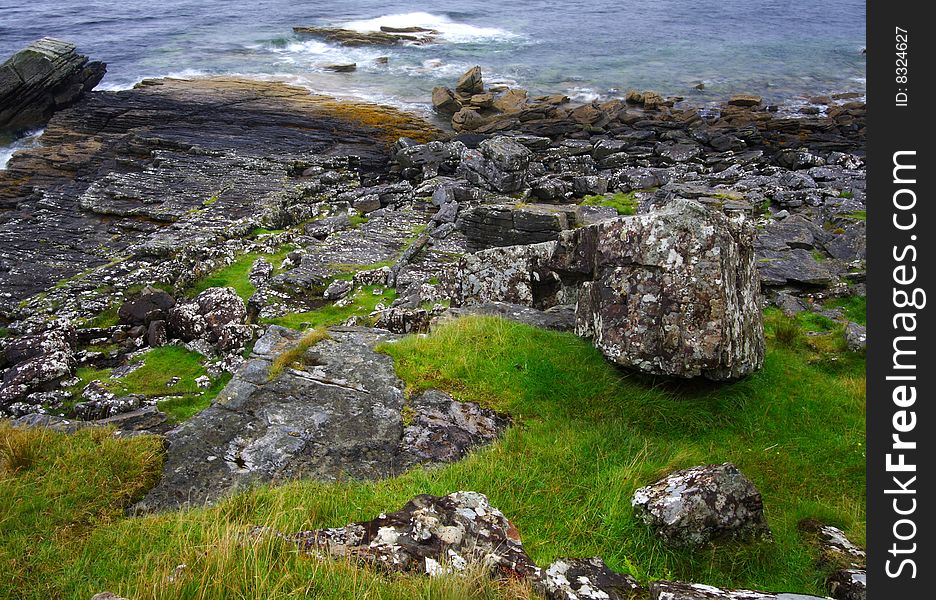 Grass, rocks and sea by a rainy and windy day at Elgol shoreline in scotland, isle of skye. Long exposure.