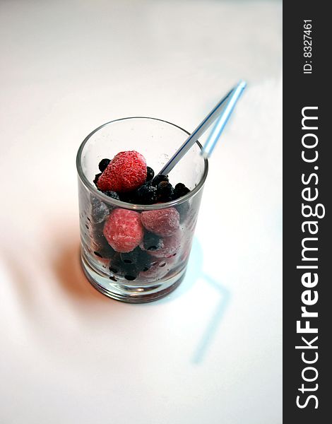 Frozen berries in glass with tube for a cocktail; frozen strawberry and currant;
 Fresh cocktail from berries