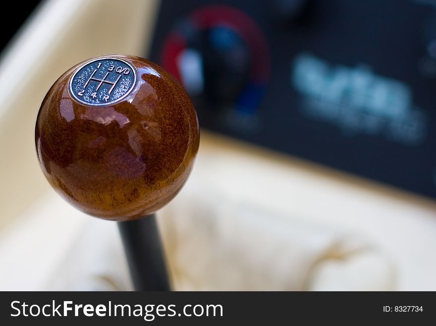 A polished wooden gear knob within a sports car, against the background of the dials of the centre console and leather of the upholstery. A polished wooden gear knob within a sports car, against the background of the dials of the centre console and leather of the upholstery