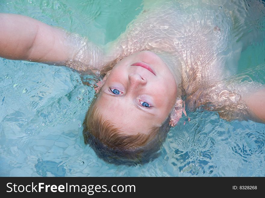 Handsome caucasian boy in pool laying back in pool looking at camera,smiling,blue eyes,blond hair. Handsome caucasian boy in pool laying back in pool looking at camera,smiling,blue eyes,blond hair