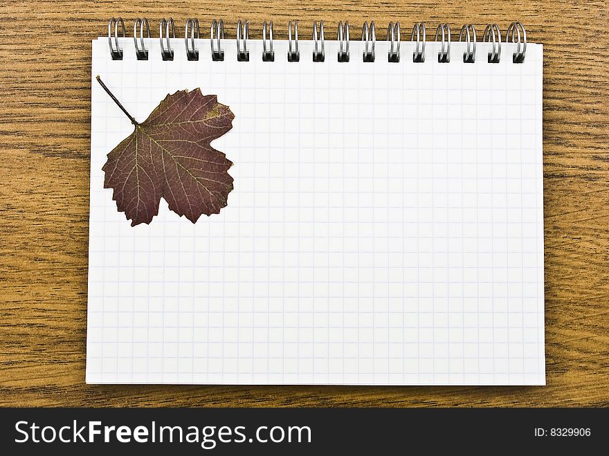 Spiral notepad  with autumn  leaf on wooden background
