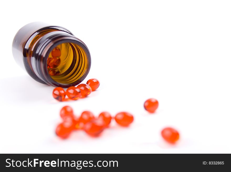 Glass bottle with red pills on white background