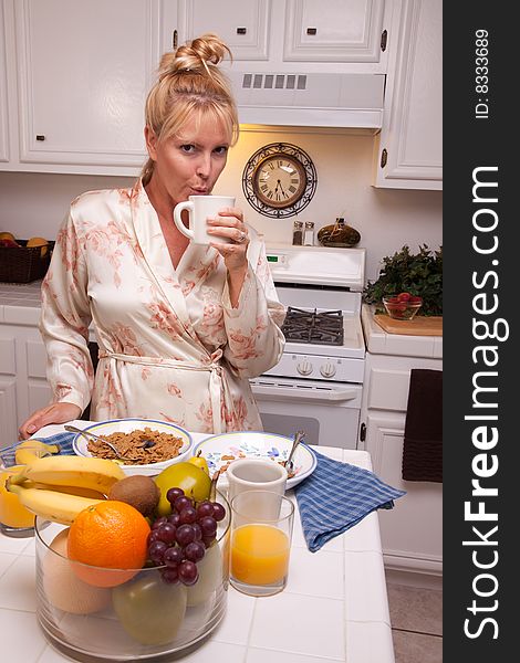 Attractive Woman In Kitchen with Fruit, Coffee, Orange Juice and Breakfast Bowls. Attractive Woman In Kitchen with Fruit, Coffee, Orange Juice and Breakfast Bowls.