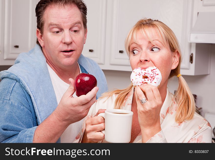 Couple in Kitchen Eating Donut and Coffee or Healthy Fruit. Couple in Kitchen Eating Donut and Coffee or Healthy Fruit.