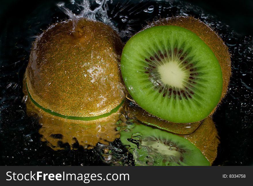 Kiwi dousing with water, with reflection, on black background