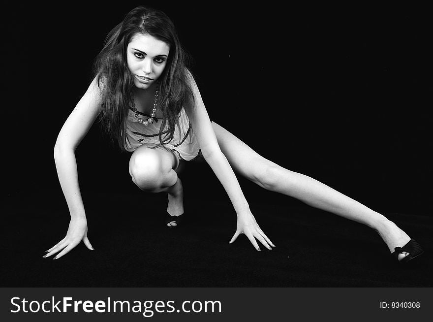 Female model stretching one leg out to her left balancing on one foot and her finger tips against a black background. Black and white image. Female model stretching one leg out to her left balancing on one foot and her finger tips against a black background. Black and white image