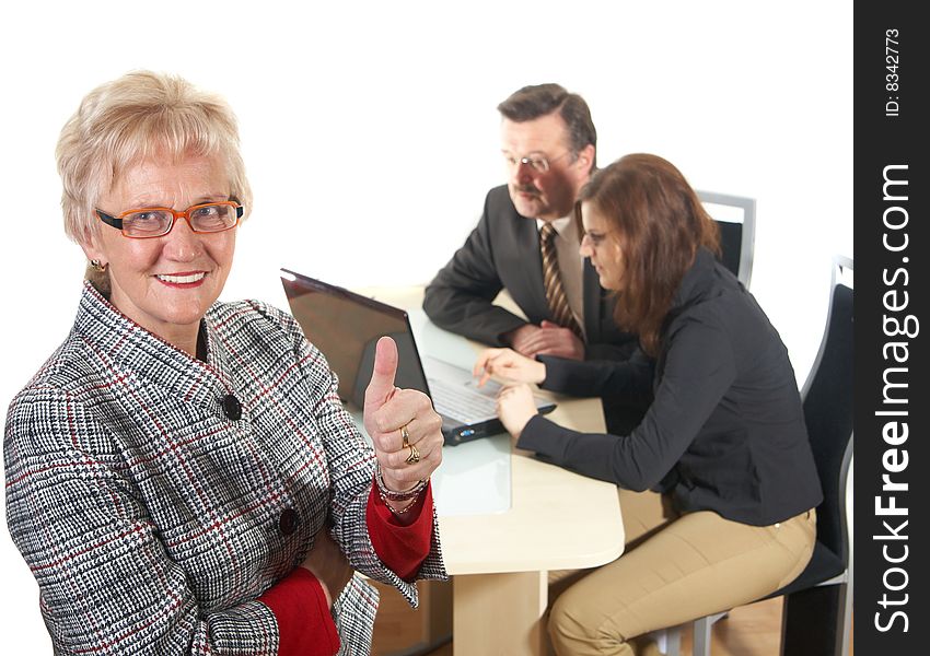 Businesswoman showing tumb up sign in office environment. Three people with focus on mature woman in front. Isolated over white. Businesswoman showing tumb up sign in office environment. Three people with focus on mature woman in front. Isolated over white.