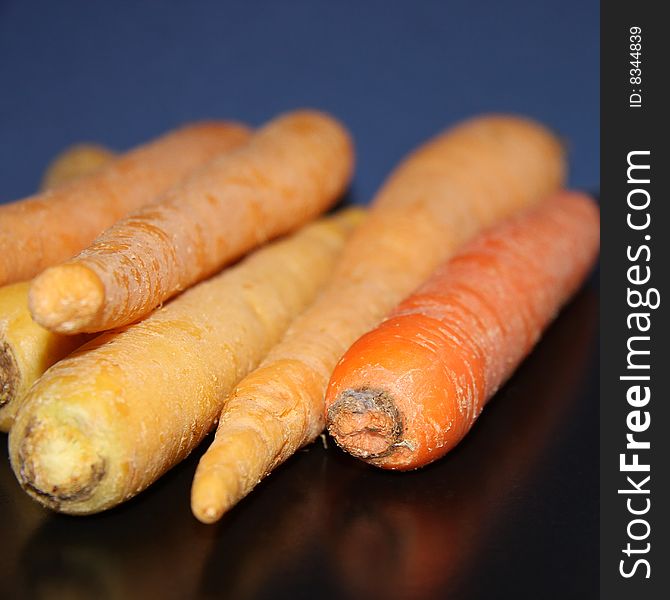 White, light orange, and deep orange raw carrots set against a blue background and on a black surface. White, light orange, and deep orange raw carrots set against a blue background and on a black surface.