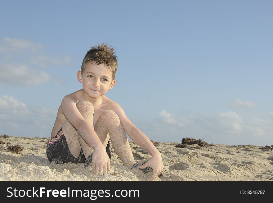A cute young boy enjoys squishing his toes in the sand. A cute young boy enjoys squishing his toes in the sand.