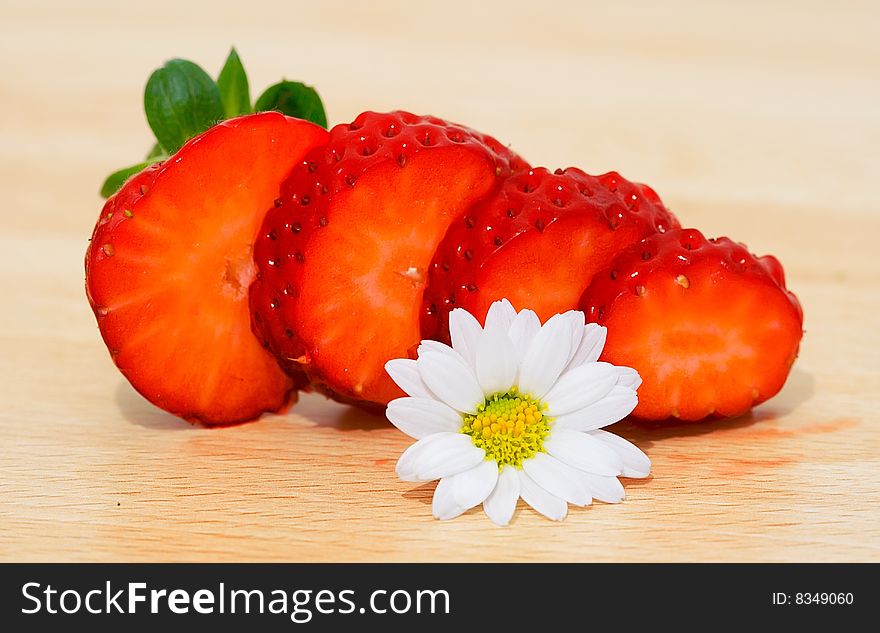 Slices of strawberry with camomile on a wood background