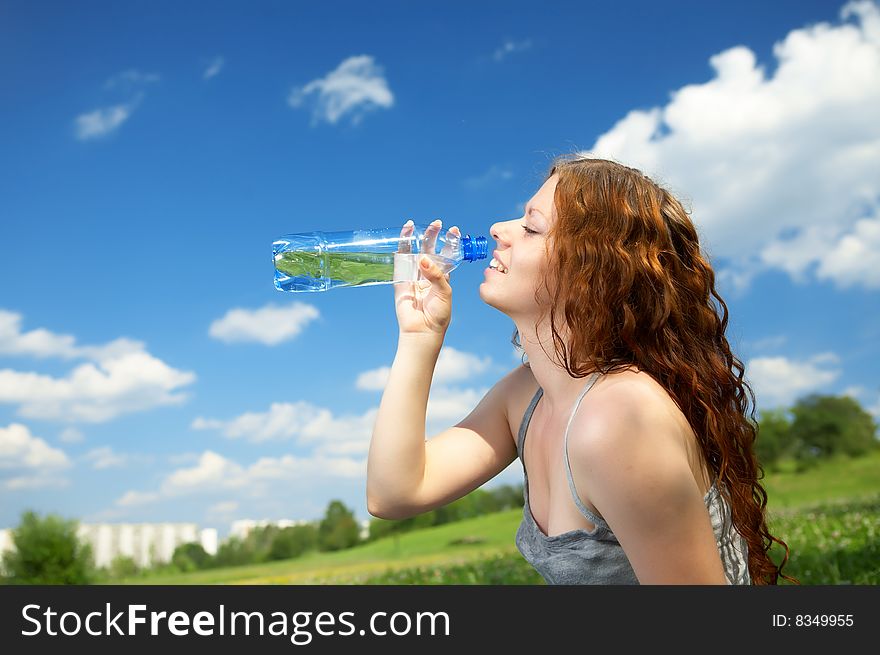 The woman in a profile drinks water from a bottle in park. The woman in a profile drinks water from a bottle in park