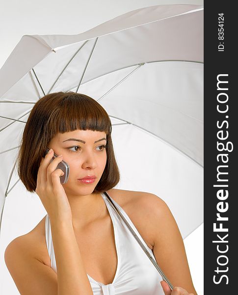 Attractive brunette in a white dress with a white umbrella and looking at the phone. Attractive brunette in a white dress with a white umbrella and looking at the phone