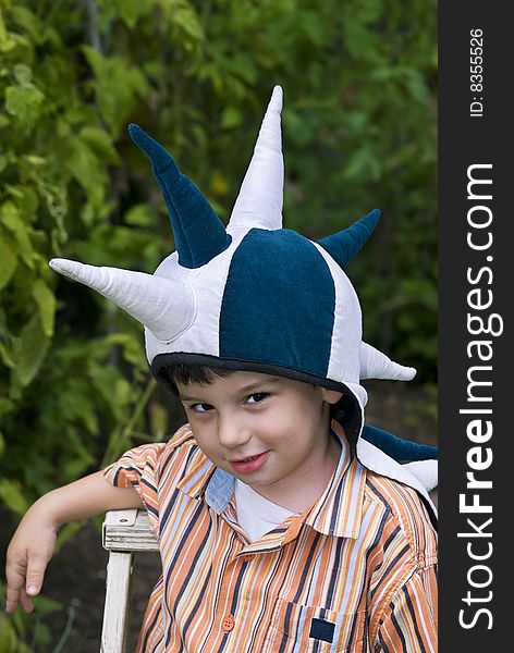 A boy strikes a mischievous pose while playing with a spiky fantasy hat. Background is a lush summer garden. A boy strikes a mischievous pose while playing with a spiky fantasy hat. Background is a lush summer garden.