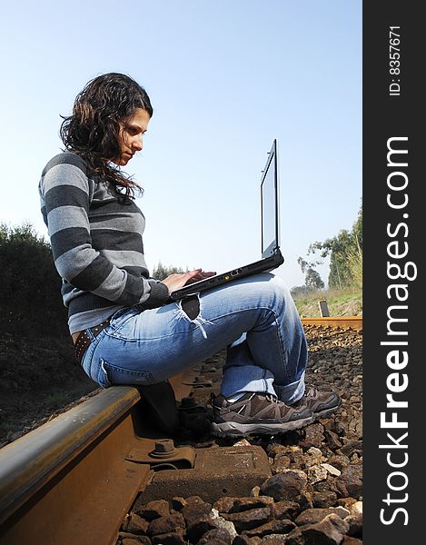 Pretty girl waiting for the train on a railway with a laptop, computer