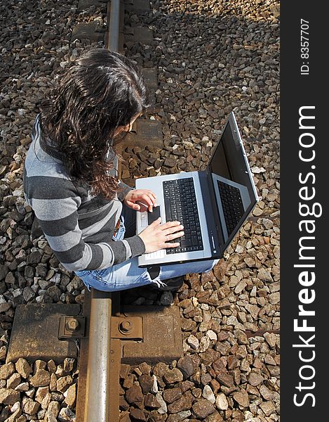 Pretty girl waiting for the train on a railway with a laptop, computer