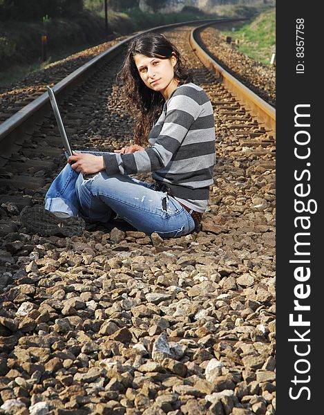 Pretty girl waiting for the train on a railway with a laptop, computer