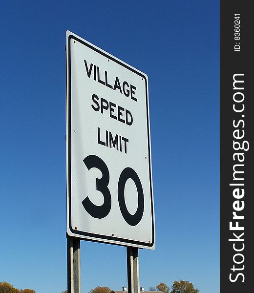 Village speed limit sign against blue sky background.