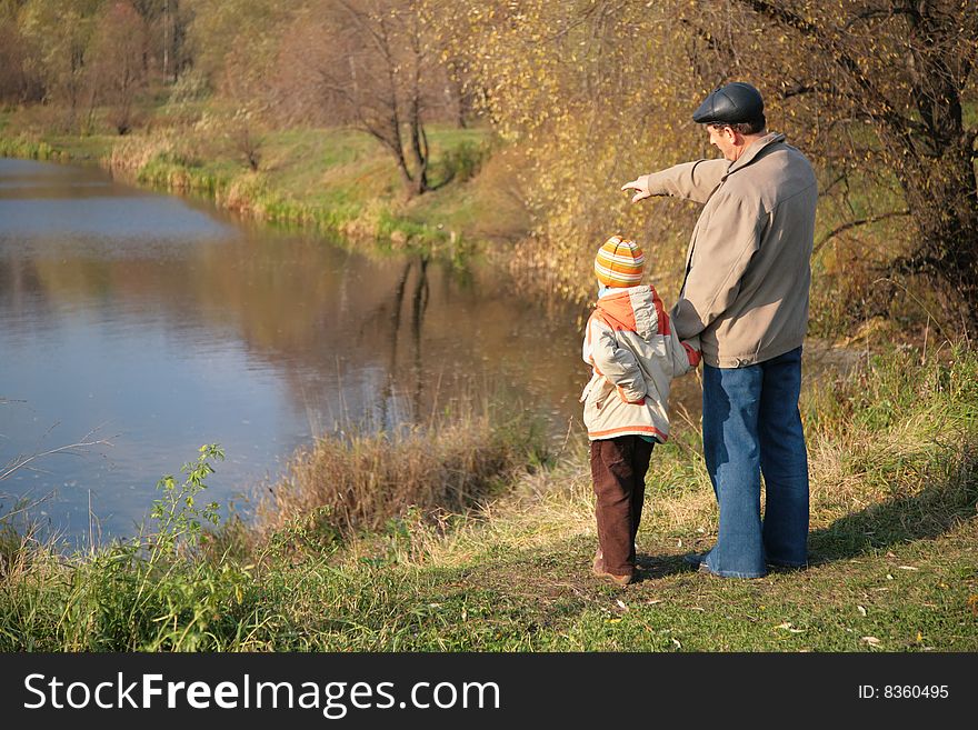 Behind grandfather with grandson in wood in autumn look on water. Behind grandfather with grandson in wood in autumn look on water