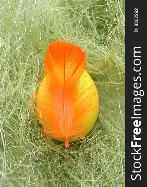 Yellow egg and orange feather on the green hay closeup. Yellow egg and orange feather on the green hay closeup