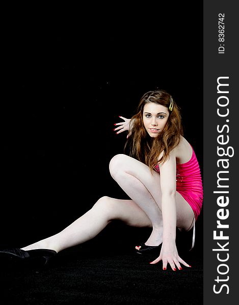 Female model wearing a bright pink top crouching against a black back ground with her fingers spread. Female model wearing a bright pink top crouching against a black back ground with her fingers spread.