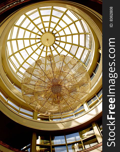 A sight of a spectacular chandelier hanging from a glass dome-shape roof; reflecting the light rays falling onto it to share it with the world and lighting up the entire hall.