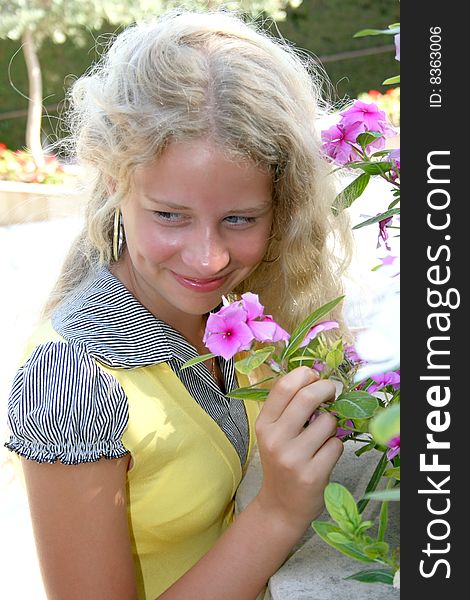 Pretty blond girl smelling pink flowers.