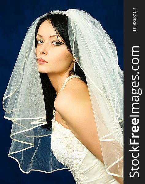Studio portrait of a beautiful brunette bride against blue background