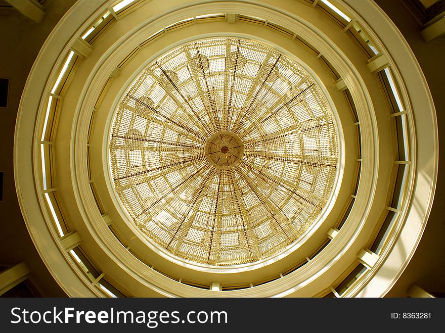 A sight of a spectacular chandelier hanging from a glass dome-shape roof; reflecting the light rays falling onto it to share it with the world and lighting up the entire hall.